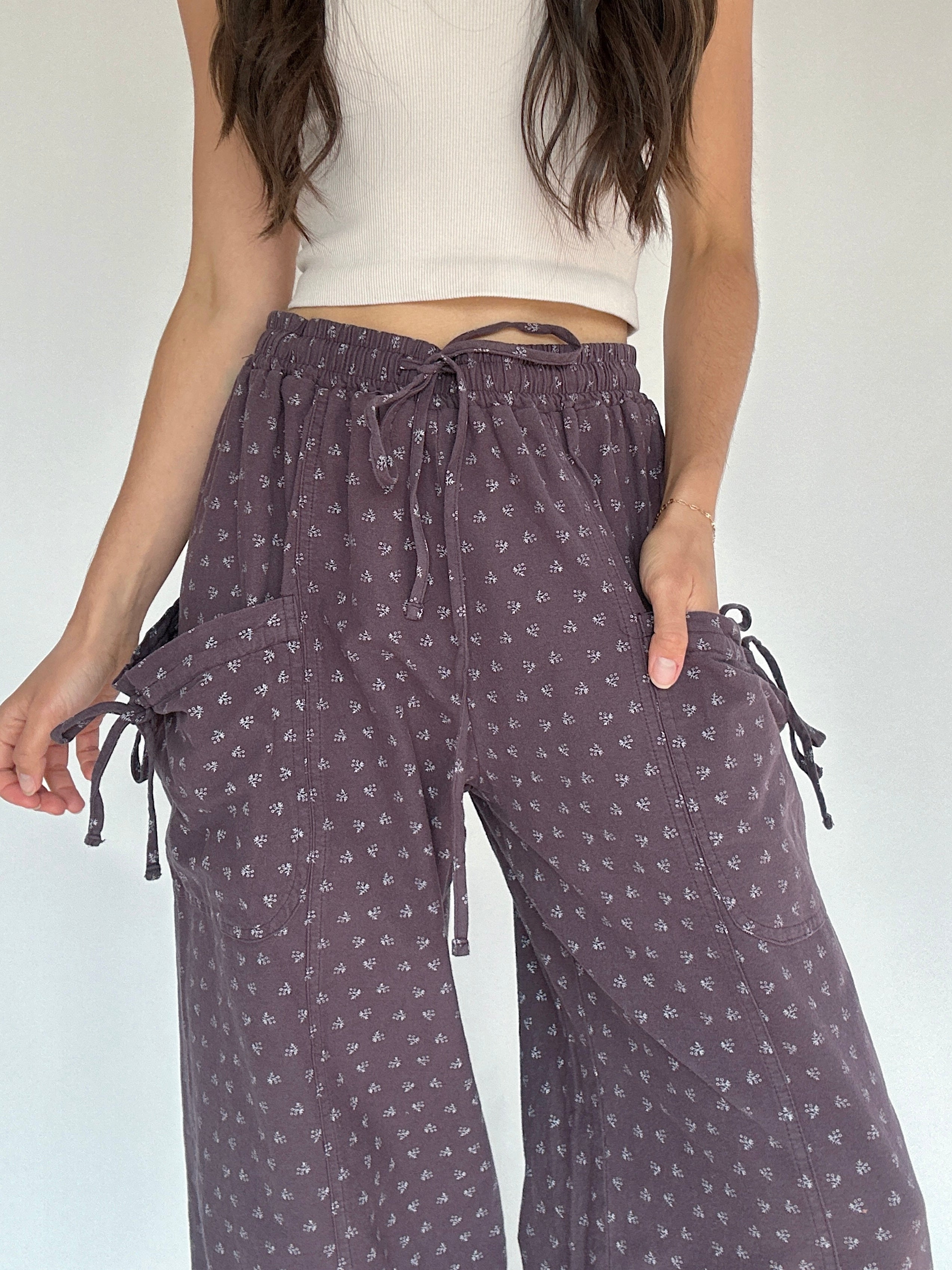 Person wearing purple patterned pants with a white top on a plain background showing up close waistband and pocket detail