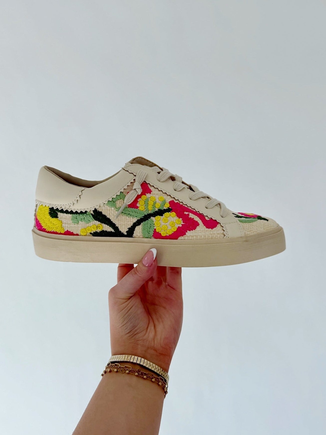 Hand holding a sneaker with floral embroidery against a light background