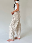 A woman wearing beige and white gingham wide-leg pants with a white t-shirt, shown from a side profile against a plain light gray studio background.
