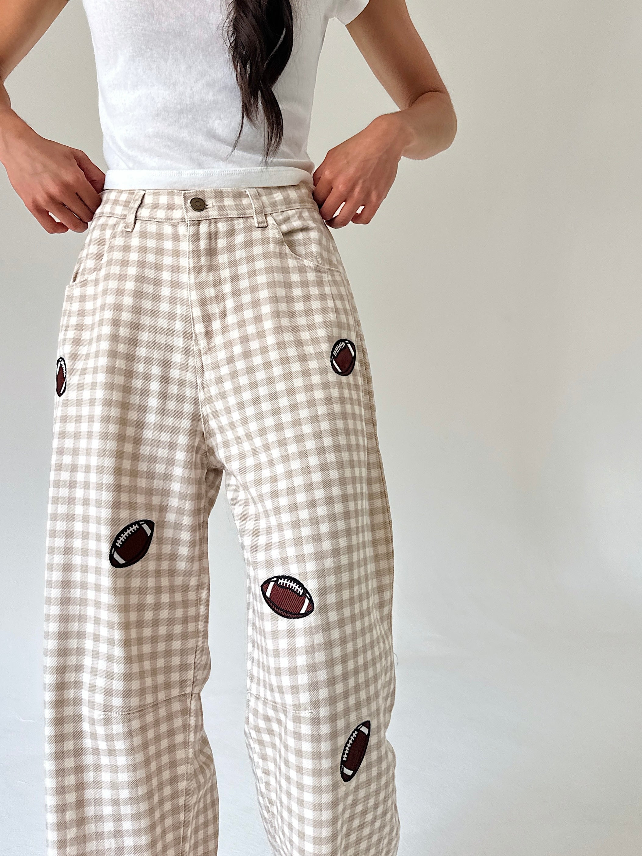 A person wearing beige and white gingham wide-leg pants with embroidered football patches, paired with a white t-shirt, shown from the waist down against a plain light background.