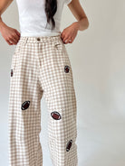 A person wearing beige and white gingham wide-leg pants with embroidered football patches, paired with a white t-shirt, shown from the waist down against a plain light background.