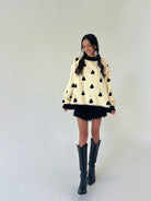 woman wearing a cream mock neck pullover with little ghost graphics all over, paired with black ruffle shorts and tall black boots