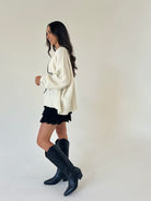 woman wearing an oversized cream sweater over lace black shorts standing from the side