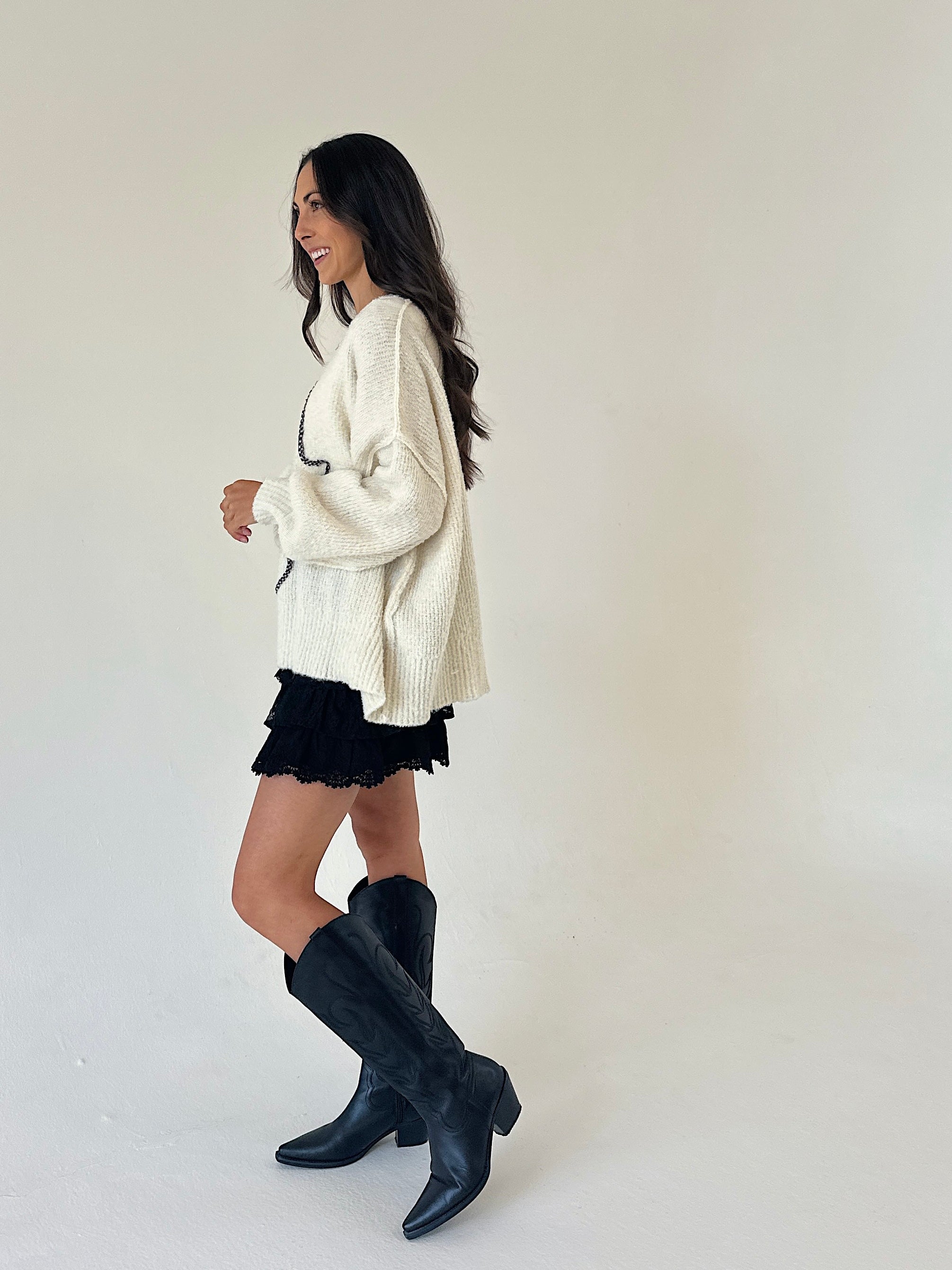 woman wearing an oversized cream sweater over lace black shorts standing from the side