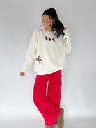 Woman wearing a cream sweatshirt with gingerbread men and candy canes with red pants on a white background