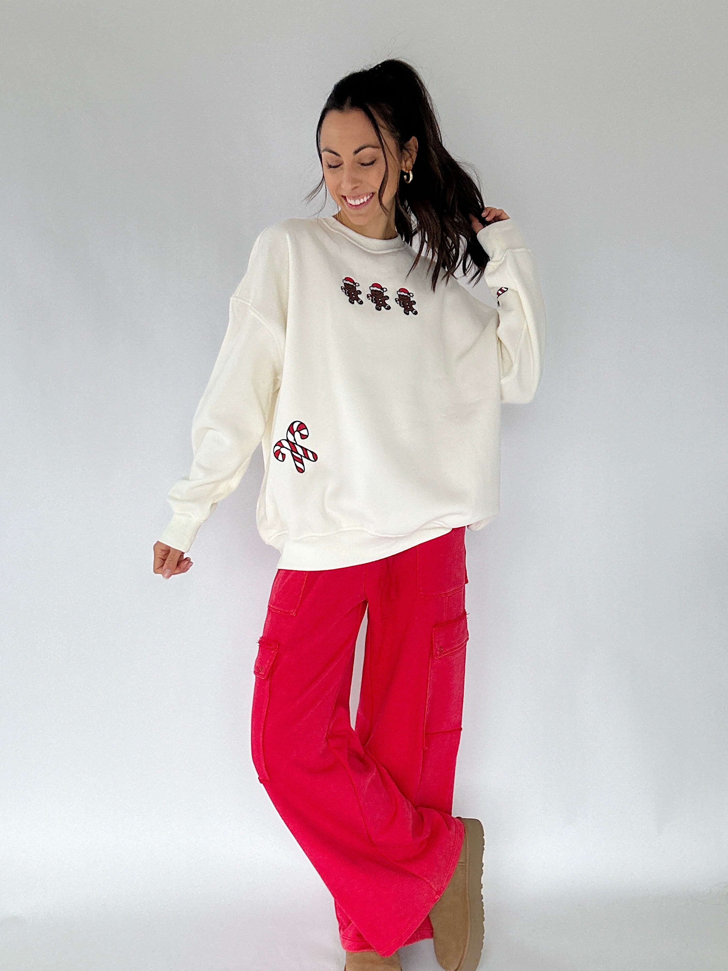 Woman wearing a cream sweatshirt with gingerbread men and candy canes with red pants on a white background