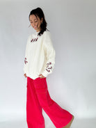 Woman wearing a white embroidered sweatshirt and red pants on a plain background