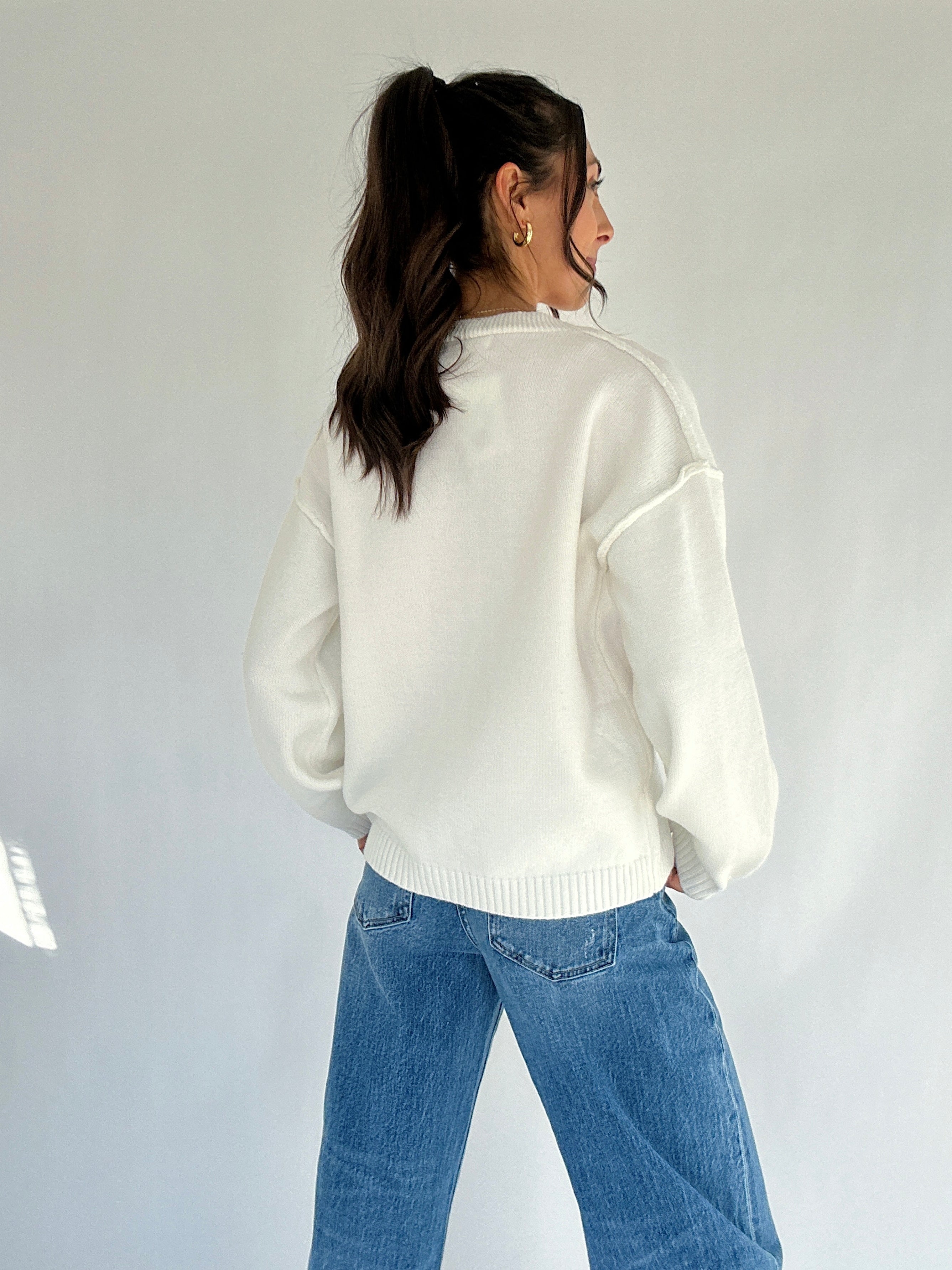 Person wearing a white sweater and blue jeans against a plain background showing back