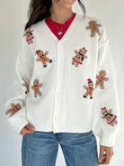 White cardigan with gingerbread man patches worn by a person on a plain background