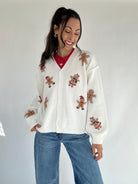 Woman wearing a white cardigan with gingerbread man patches on a plain background