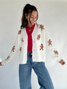 Woman wearing a white sweater with gingerbread man patches on a plain background