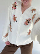 Person wearing a white cardigan with gingerbread man patterns on a plain background
