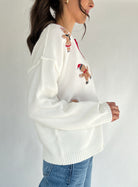 White sweater with gingerbread men embroidery worn by a person on a plain background
