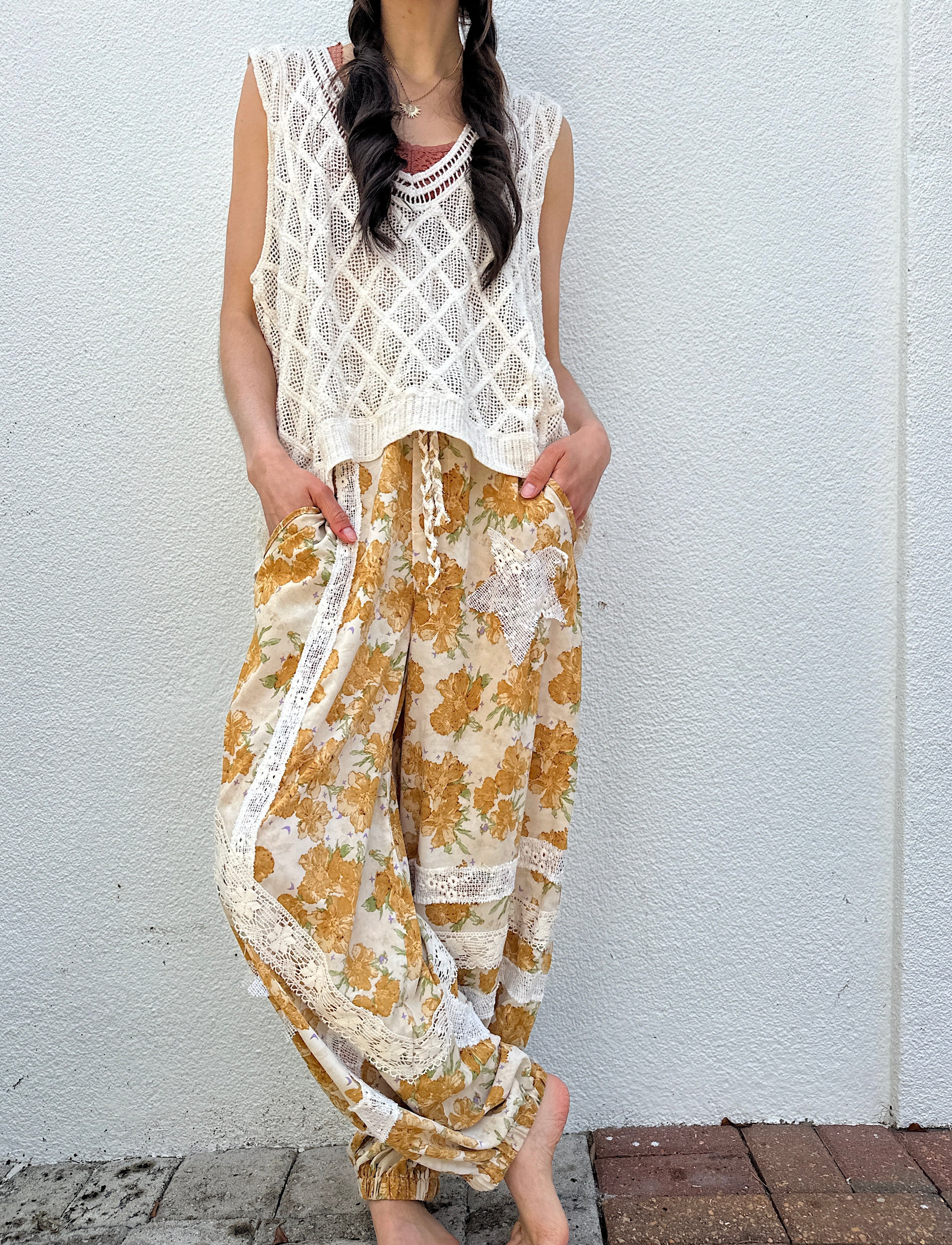 Person wearing a white lace top and yellow floral pants against a white wall.