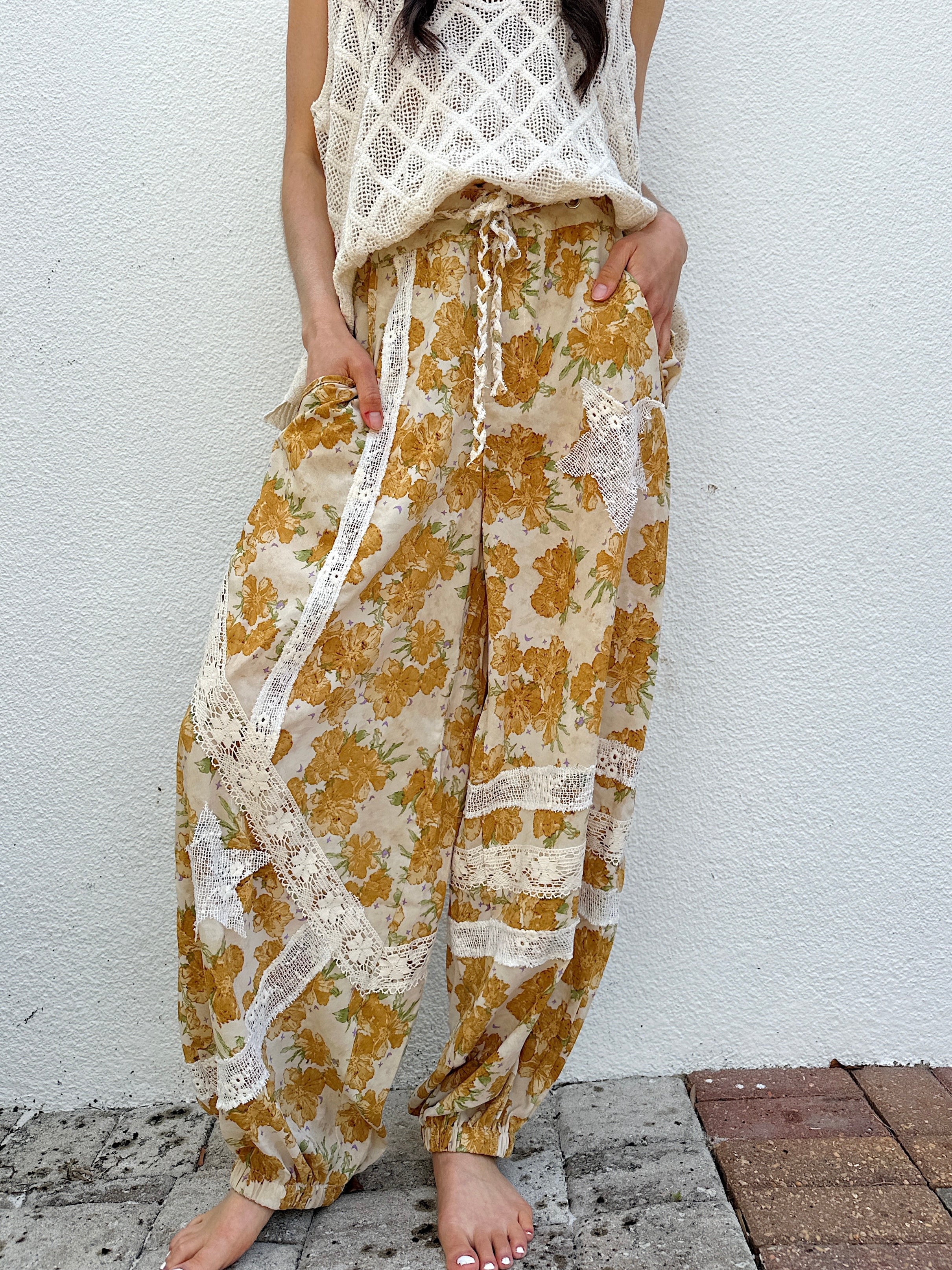 Person wearing floral pants with lace details against a white wall.