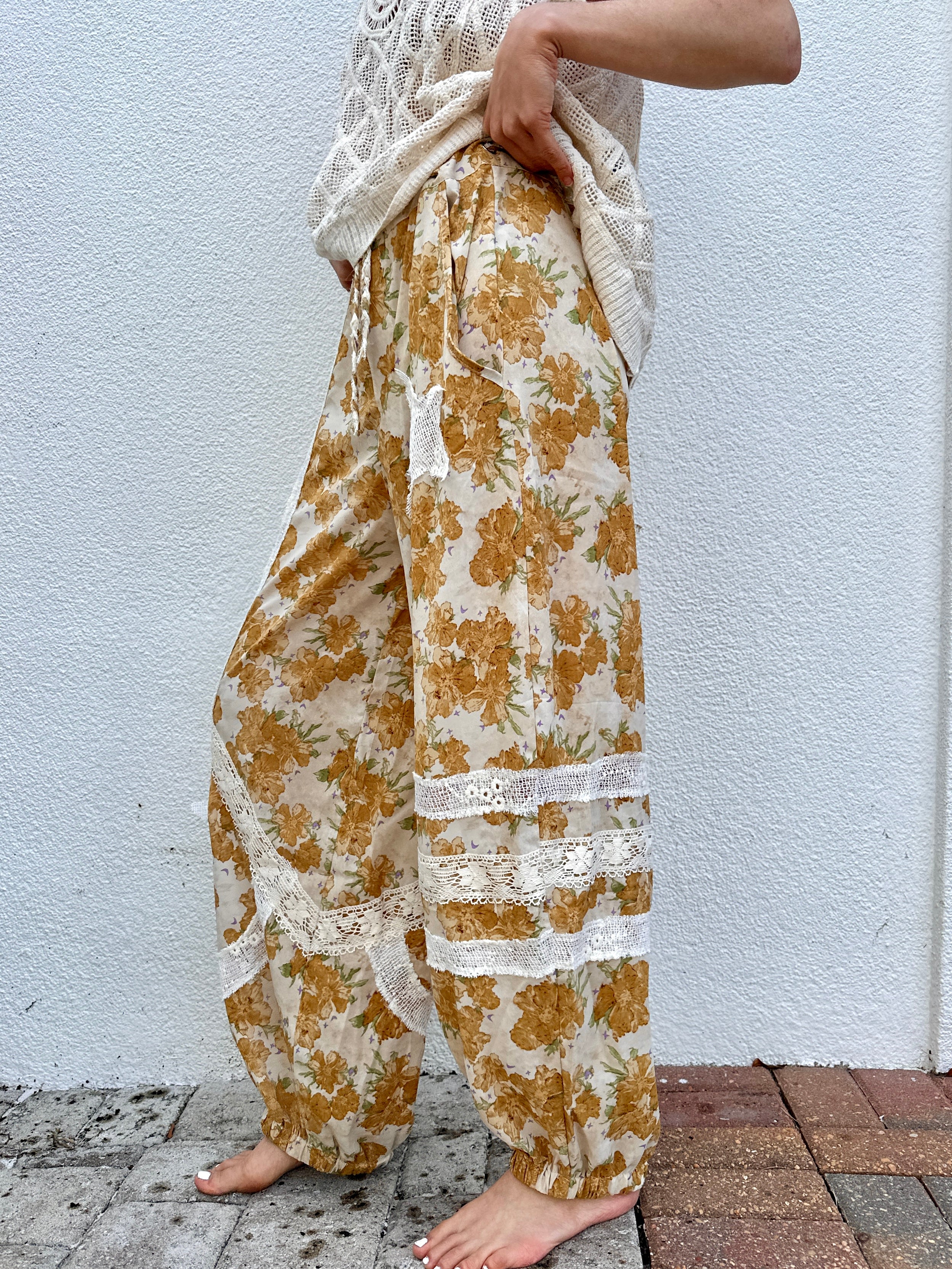 Person wearing floral pants with lace details against a white wall from side