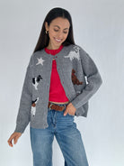 Woman wearing a gray cardigan with dog graphics over a red tee and jeans on a plain background