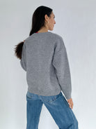 Person wearing a gray sweater and blue jeans on a white background showing the back