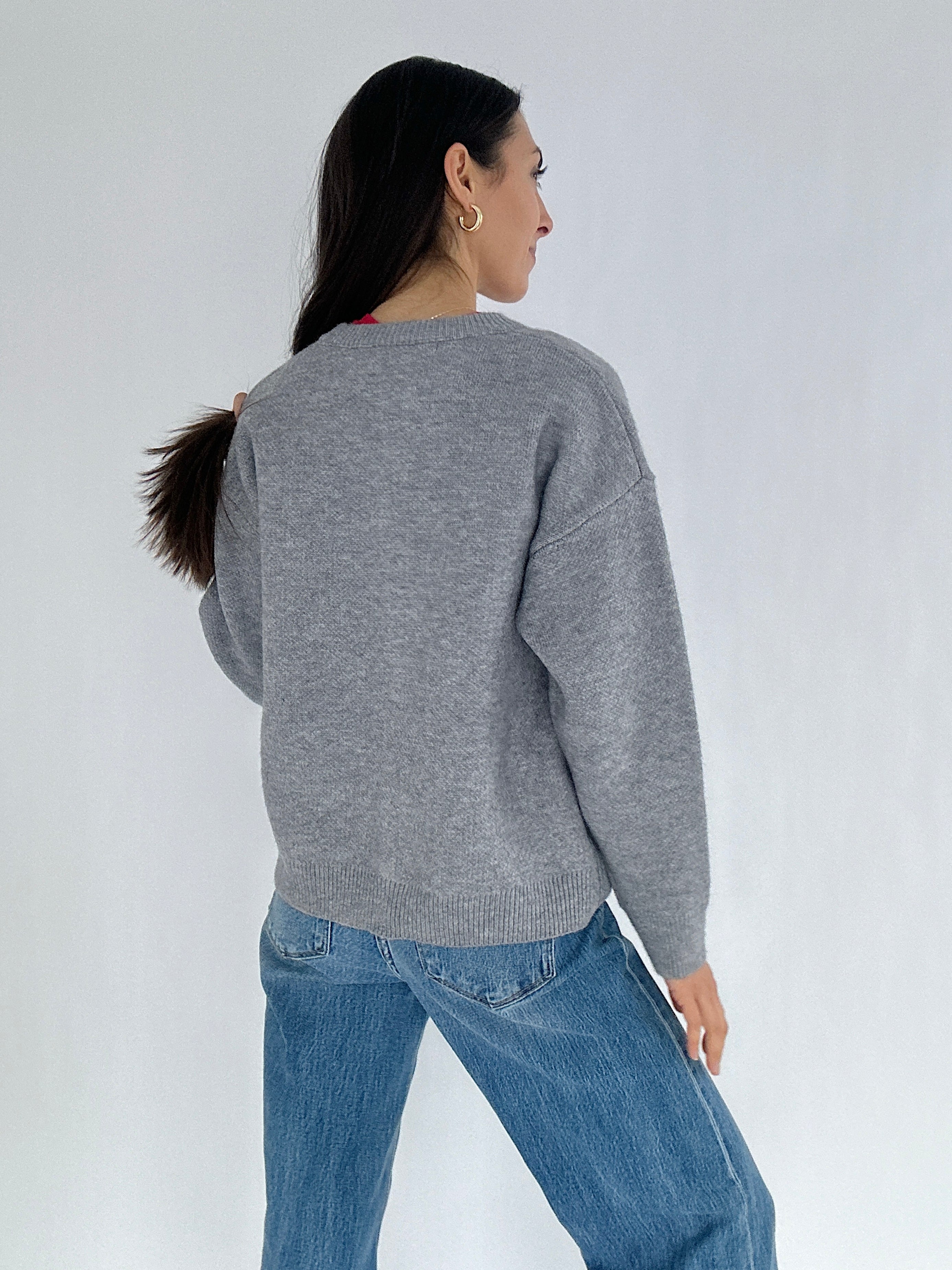 Person wearing a gray sweater and blue jeans on a white background showing the back