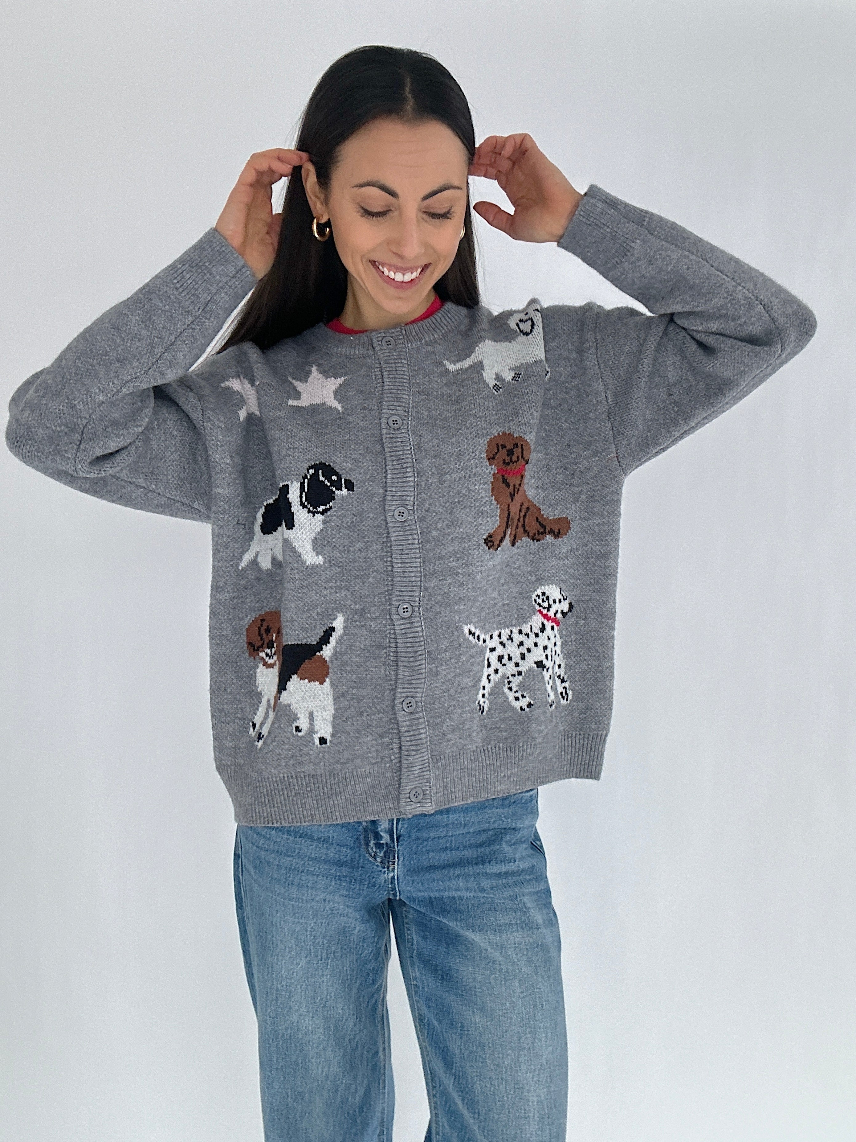 Woman wearing a gray cardigan sweater with dog illustrations buttoned with jeans on a white background