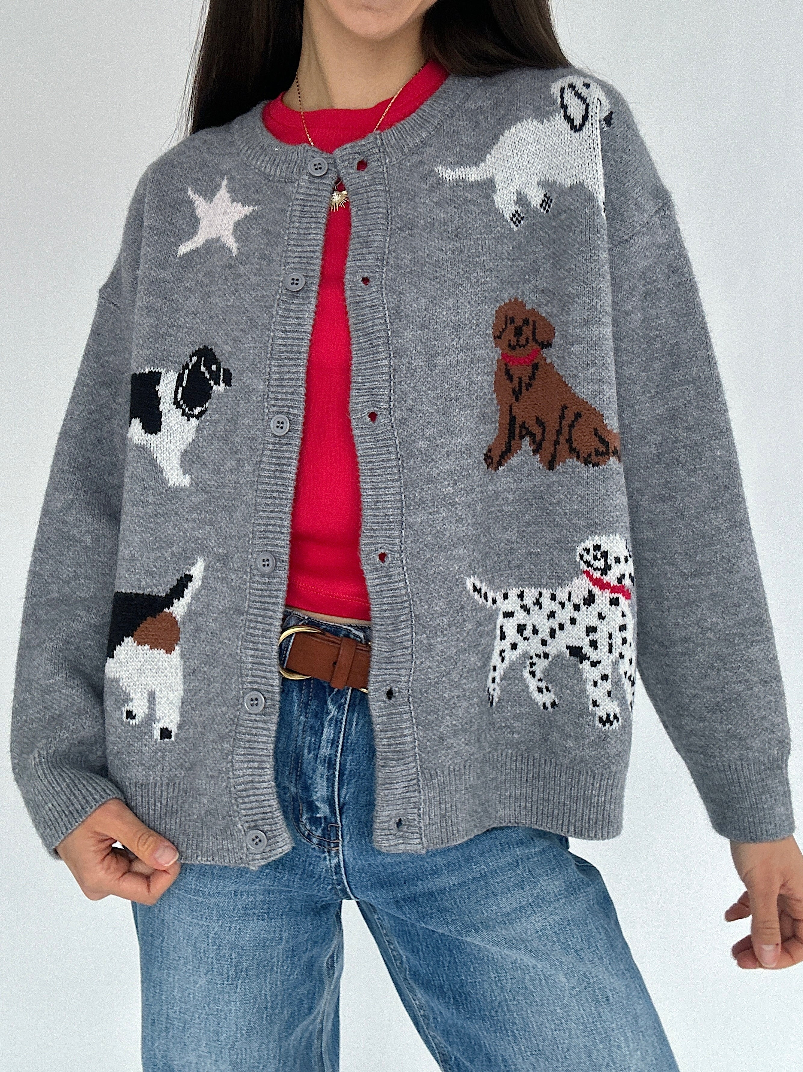 Person wearing a gray cardigan with dog patterns over a red tee on a plain background