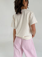 Person wearing a beige t-shirt and pink checkered pants on a plain background from back