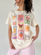 Person wearing a cream-colored t-shirt with colorful stamp designs on a plain background