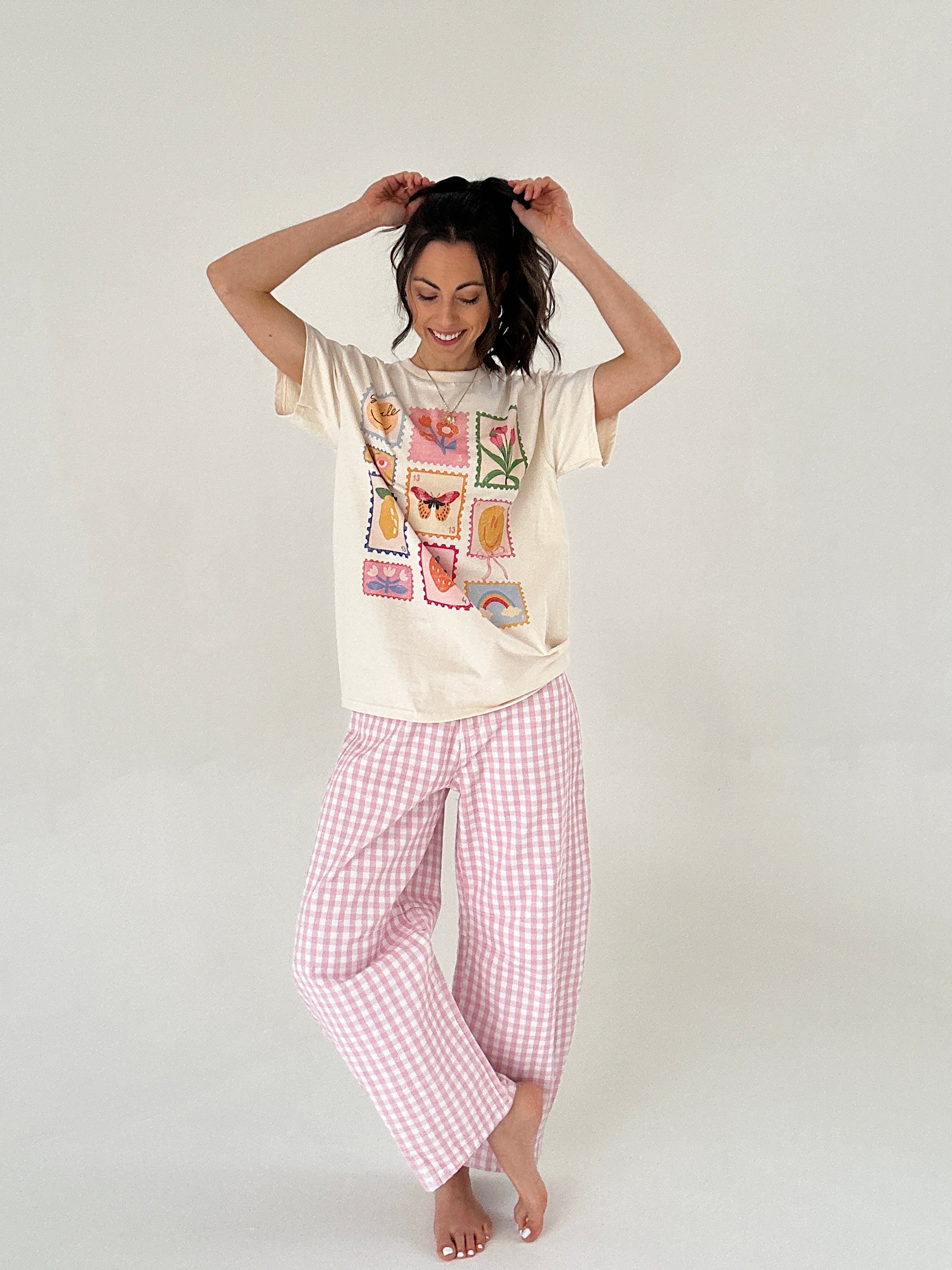 Woman wearing a graphic tee with a colorful stamp design and pink checkered pants on a white background