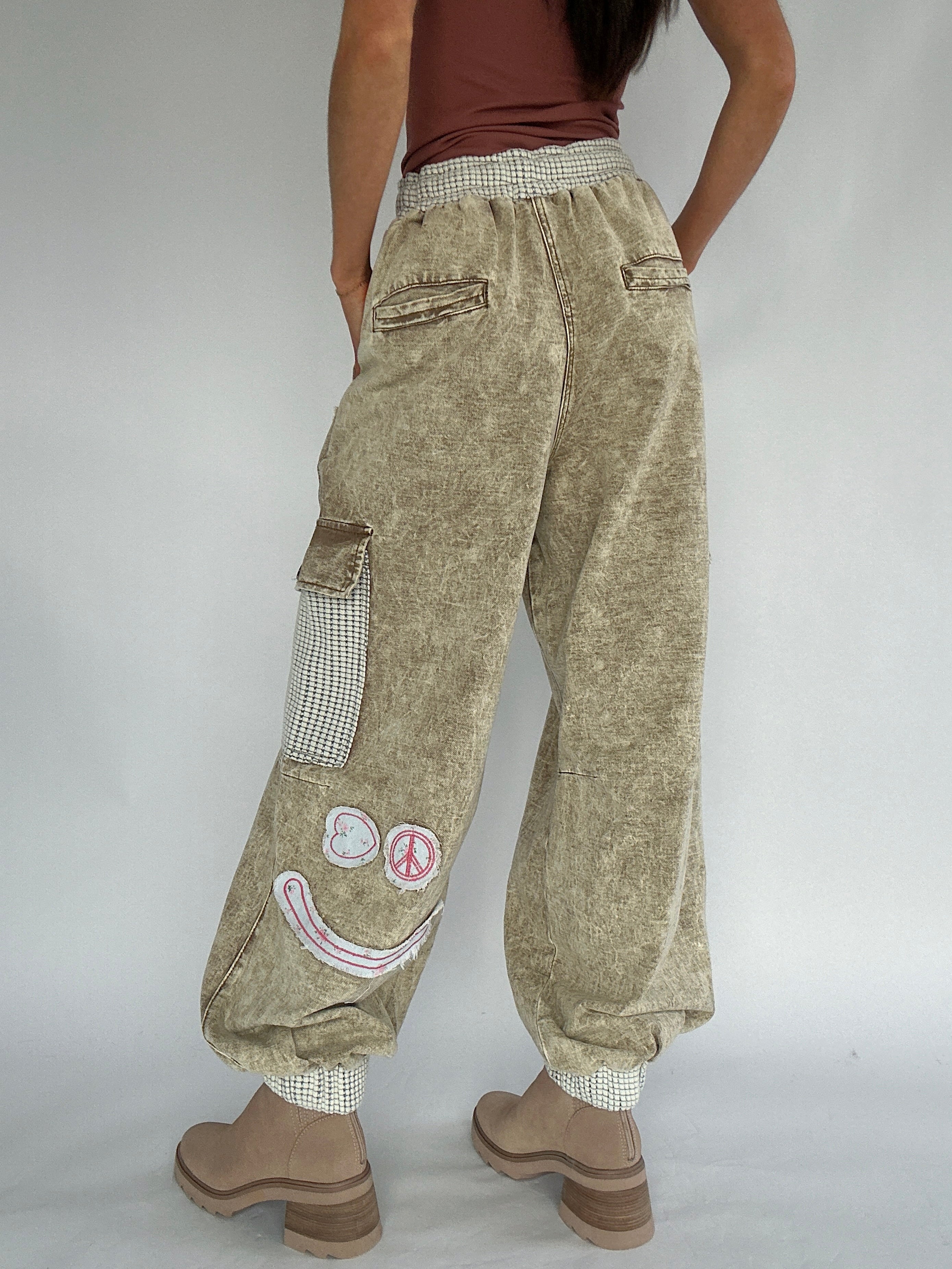 Person wearing beige cargo pants with smiley patches on a plain background from back