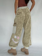 Person wearing beige cargo pants with smiley patches on a plain background from back