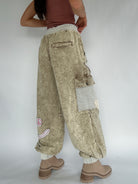 Person wearing beige cargo pants with patches on a plain background