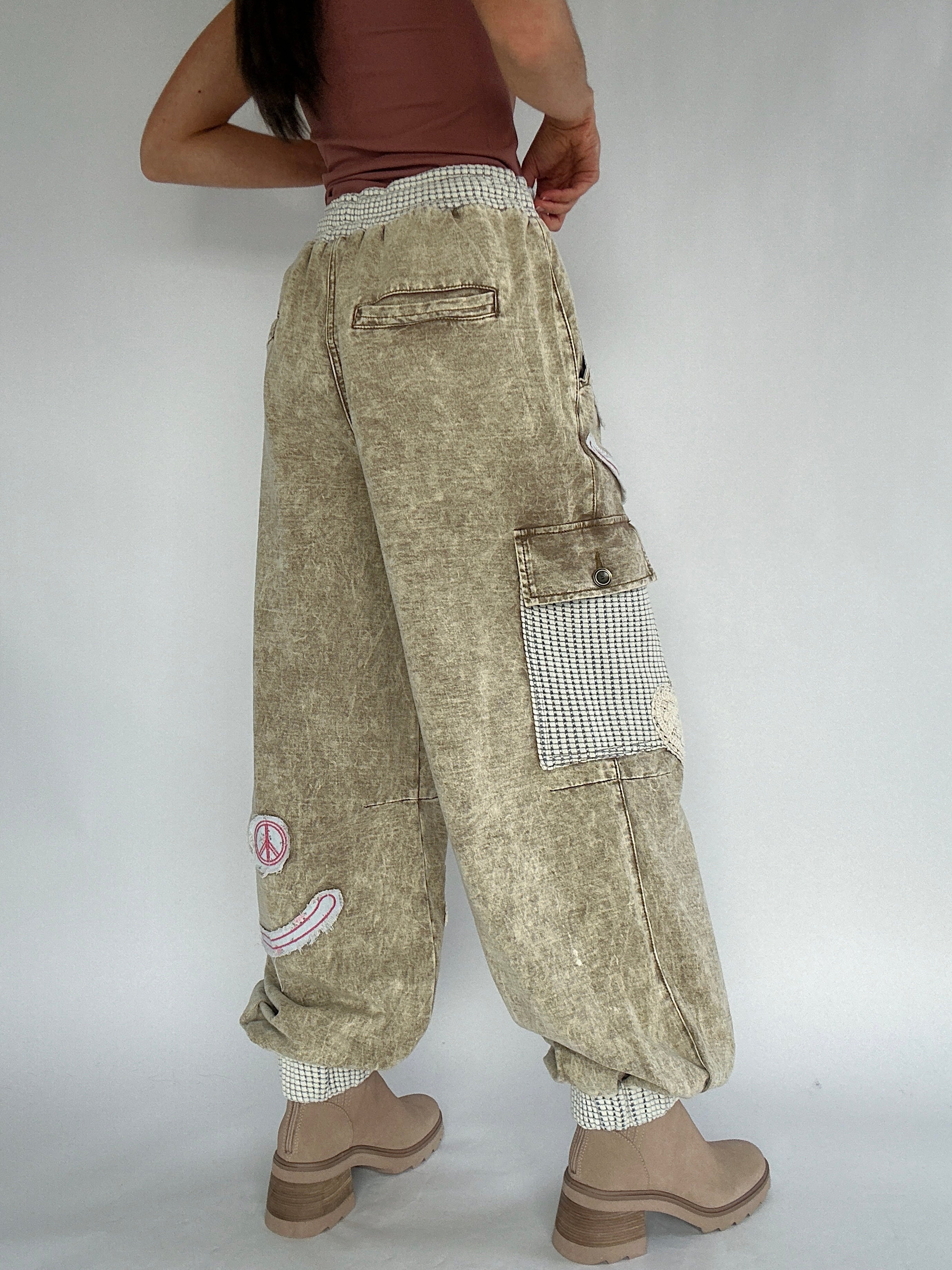 Person wearing beige cargo pants with patches on a plain background