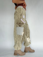 Person wearing beige patchwork jogger pants with a plain background from side