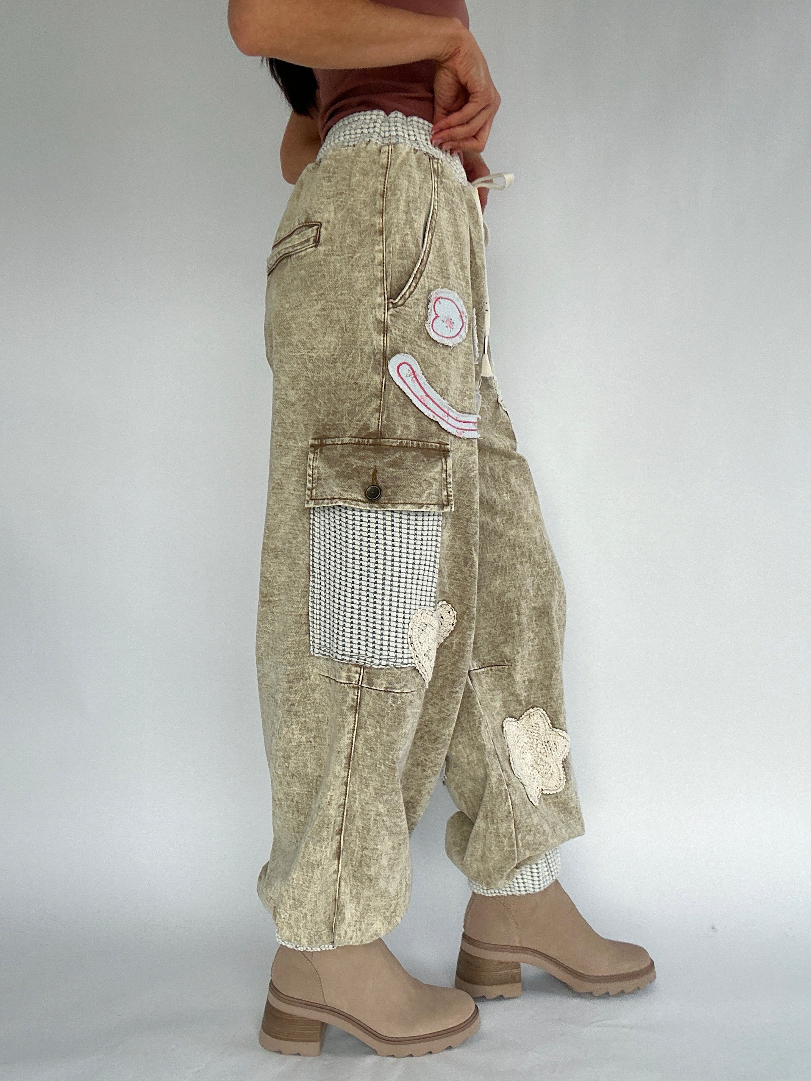 Person wearing beige patchwork jogger pants with a plain background from side