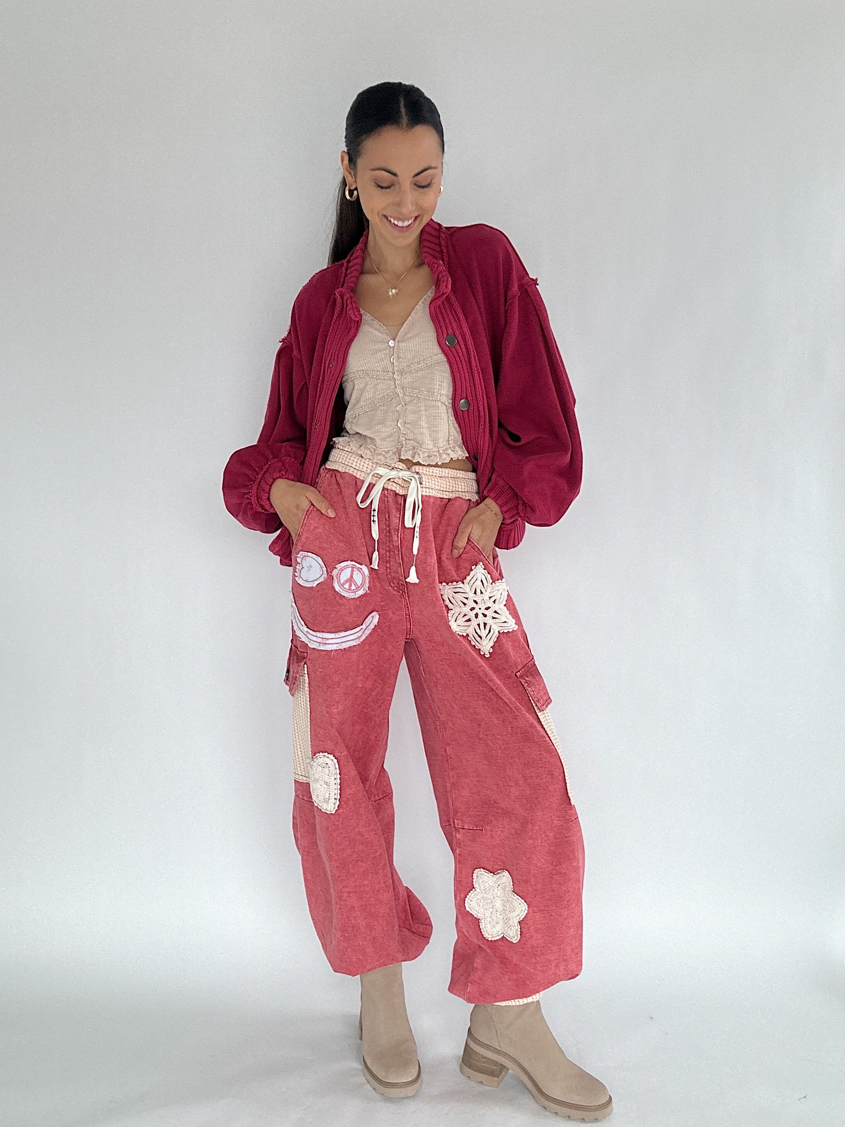 Woman wearing a red jogger style pants with whimsical patches with a red cardigan on a white background