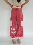 Person wearing red cargo pants with smiley face design on a plain background