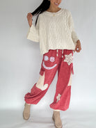 Person wearing a cream cable knit sweater and red pants with smiley face designs on a white background