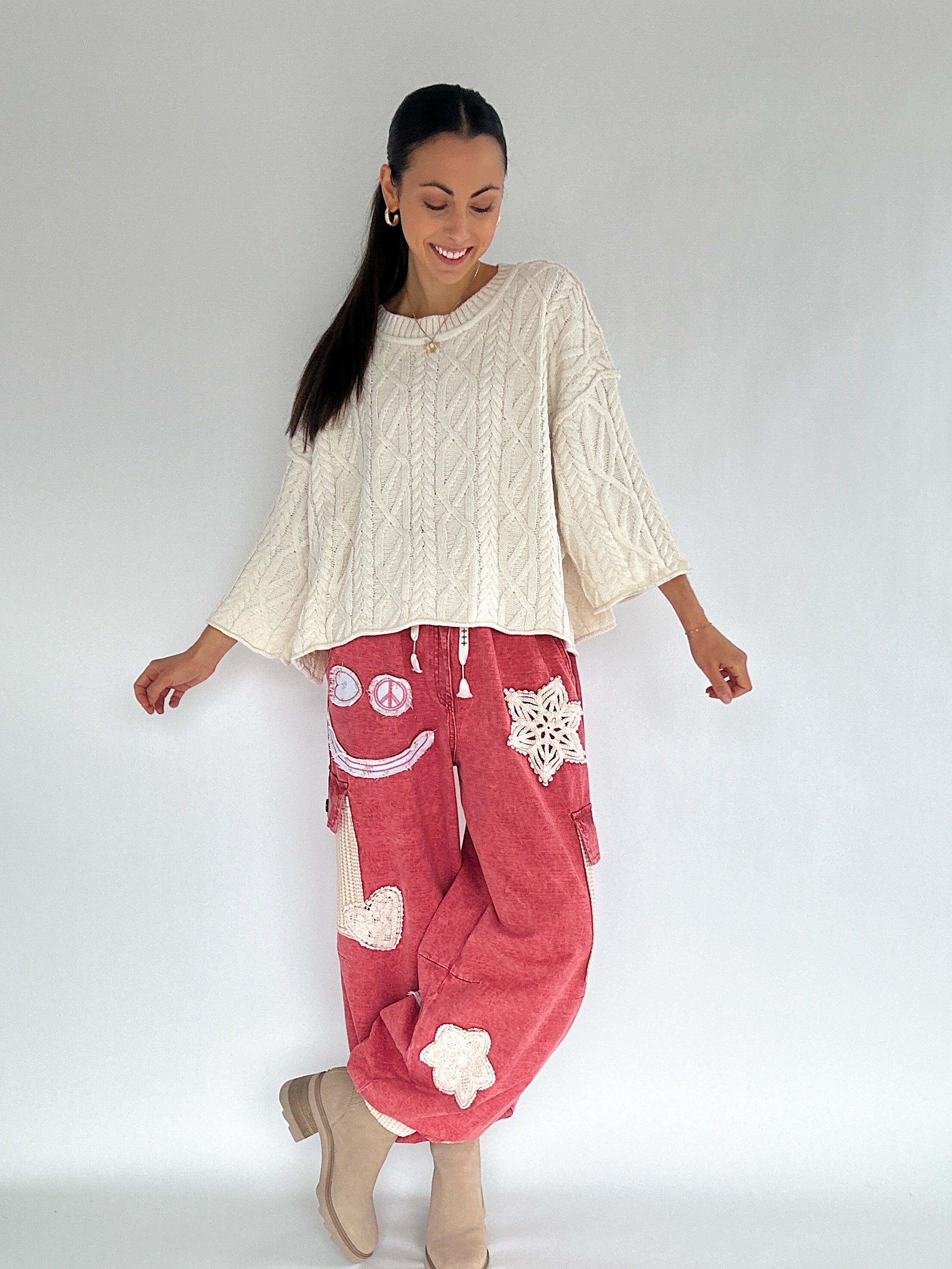 Woman wearing a cream sweater and red pants with patterns on a plain background