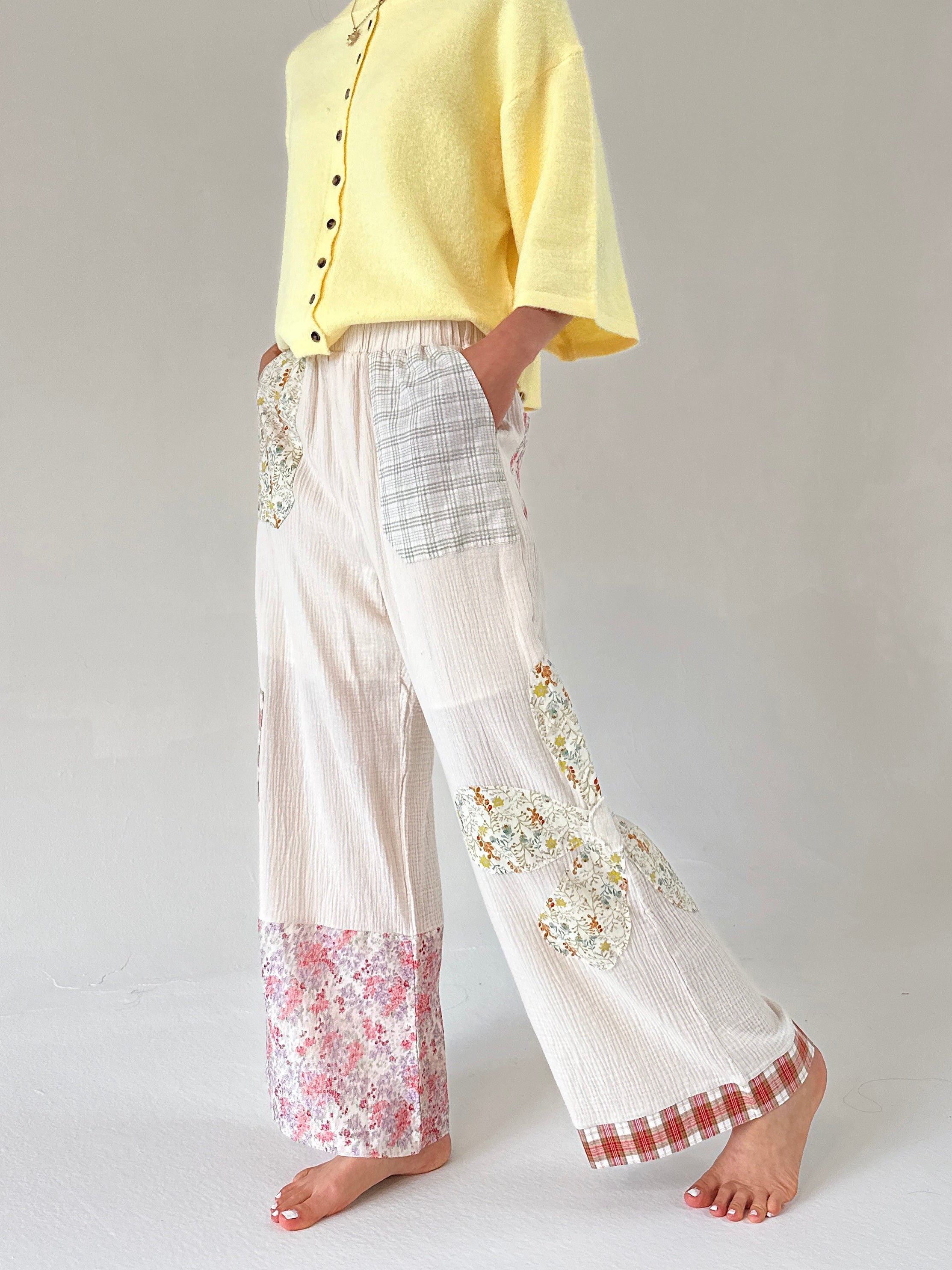 Person wearing a yellow top and white pants with floral and checkered patterns on a plain background