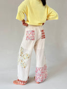 Person wearing a yellow top and floral patchwork pants on a plain background