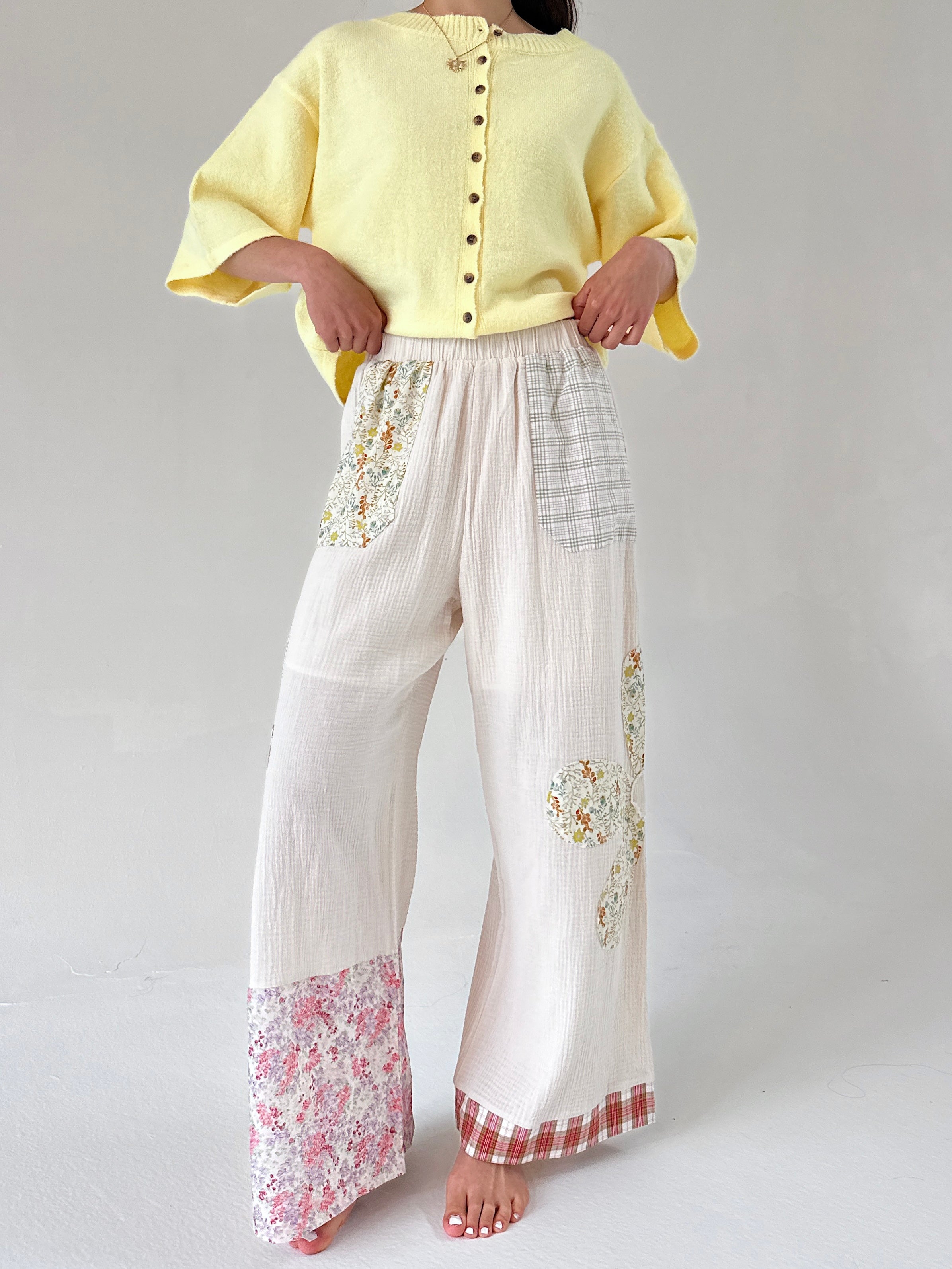 Person wearing a yellow top and white pants with floral patterns on a plain background