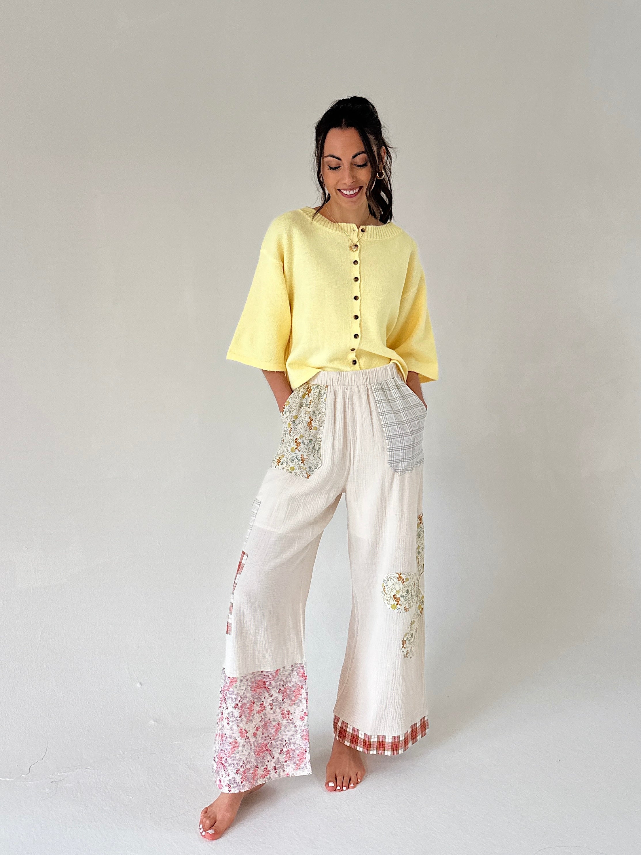 Woman wearing a yellow top and white pants with floral patterns on a plain background