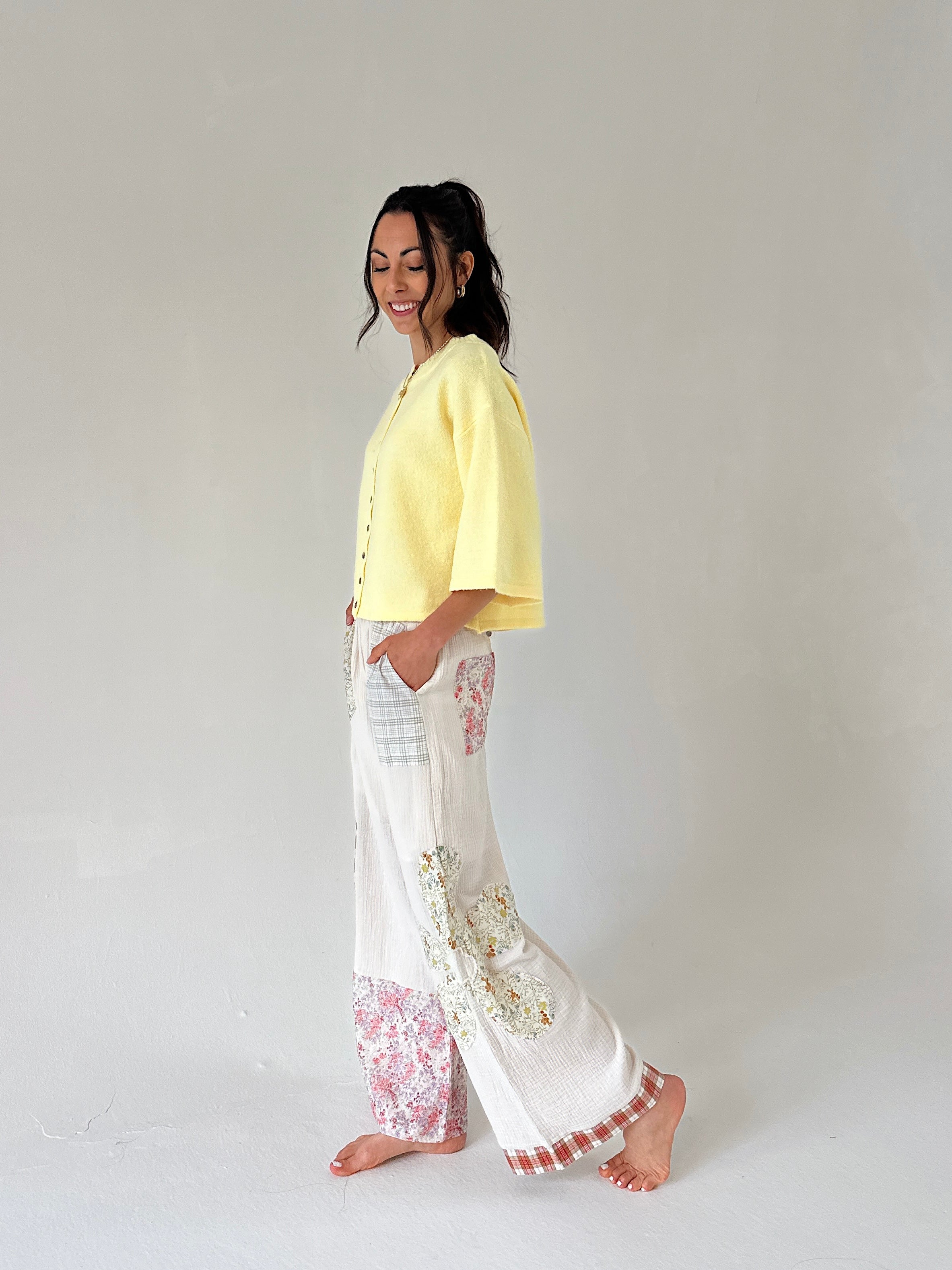 Woman wearing a yellow top and white pants with floral patterns on a plain background