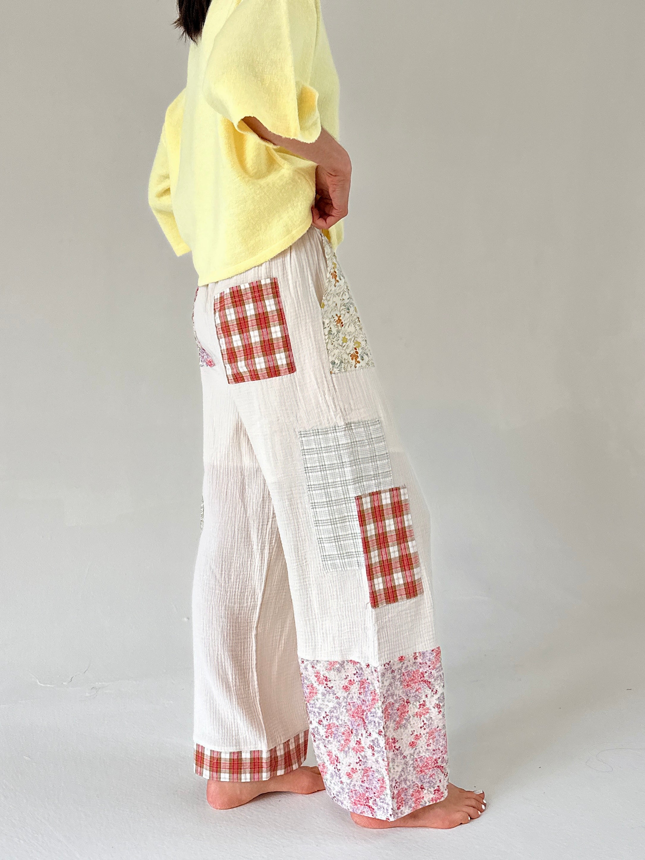 Person wearing a yellow top and white pants with red and white checkered and floral patches on a plain background from side