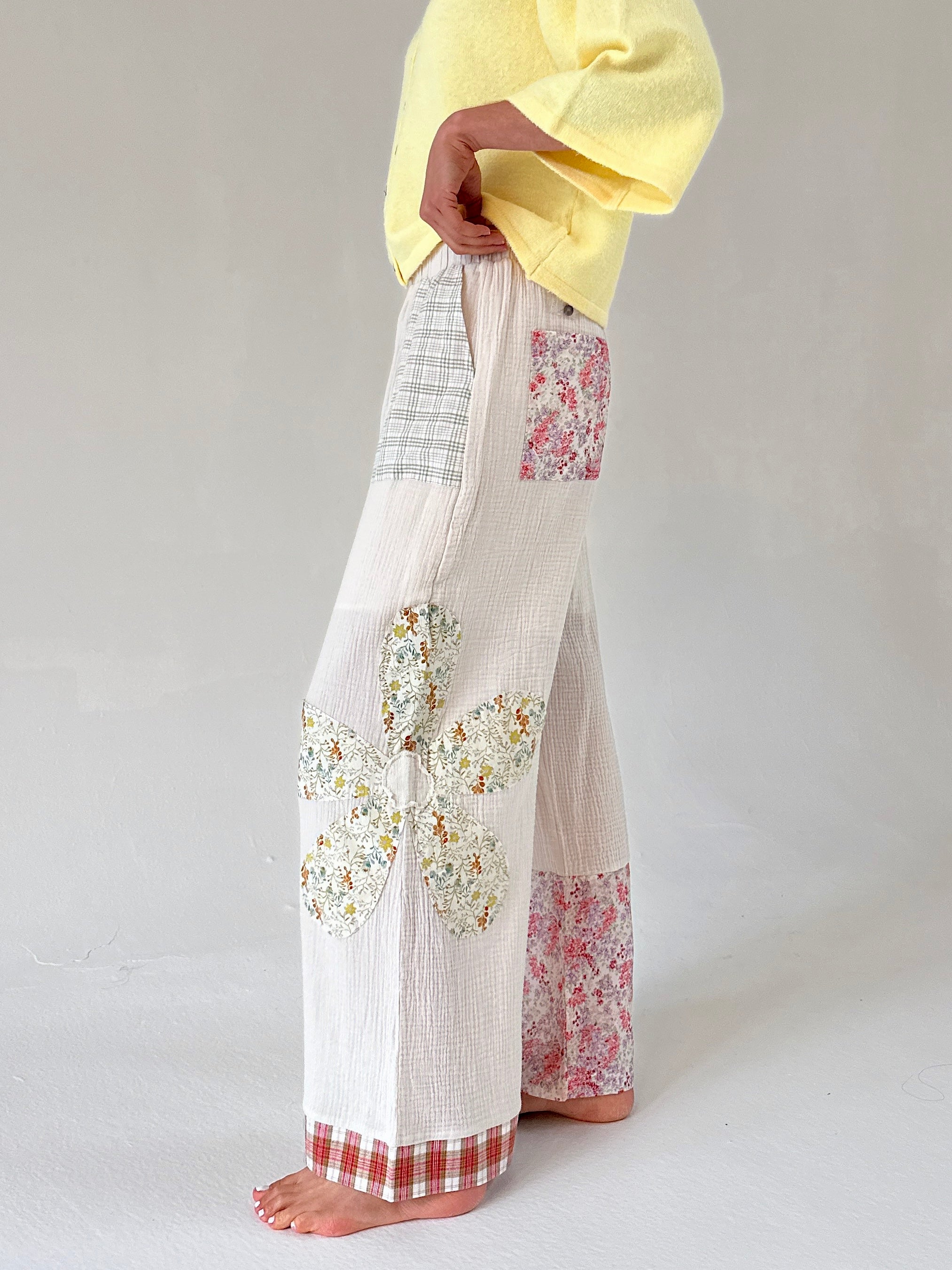 Person wearing white pants with floral patterns on a plain background from side