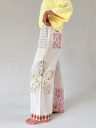 Person wearing white pants with floral patterns on a plain background from side