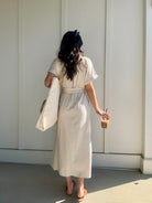 woman wearing oatmeal linen maxi dress from the back. she is holding a coffee and carrying a tote