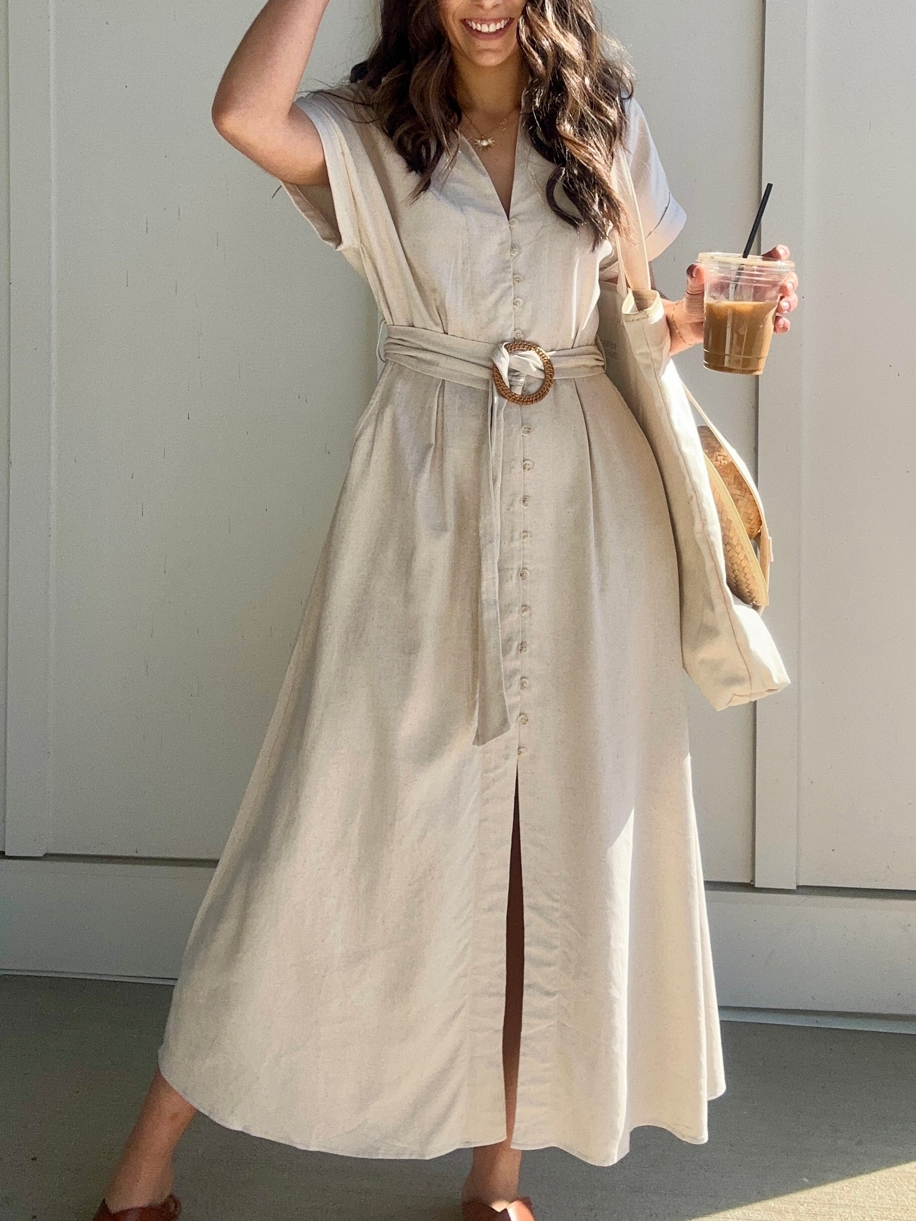 Oatmeal linen maxi dress with button down front and waist belt. Woman is holding a coffee.