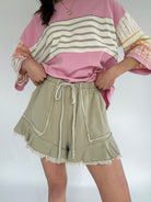 Person wearing a pink and striped long-sleeve top with olive green shorts on a white background