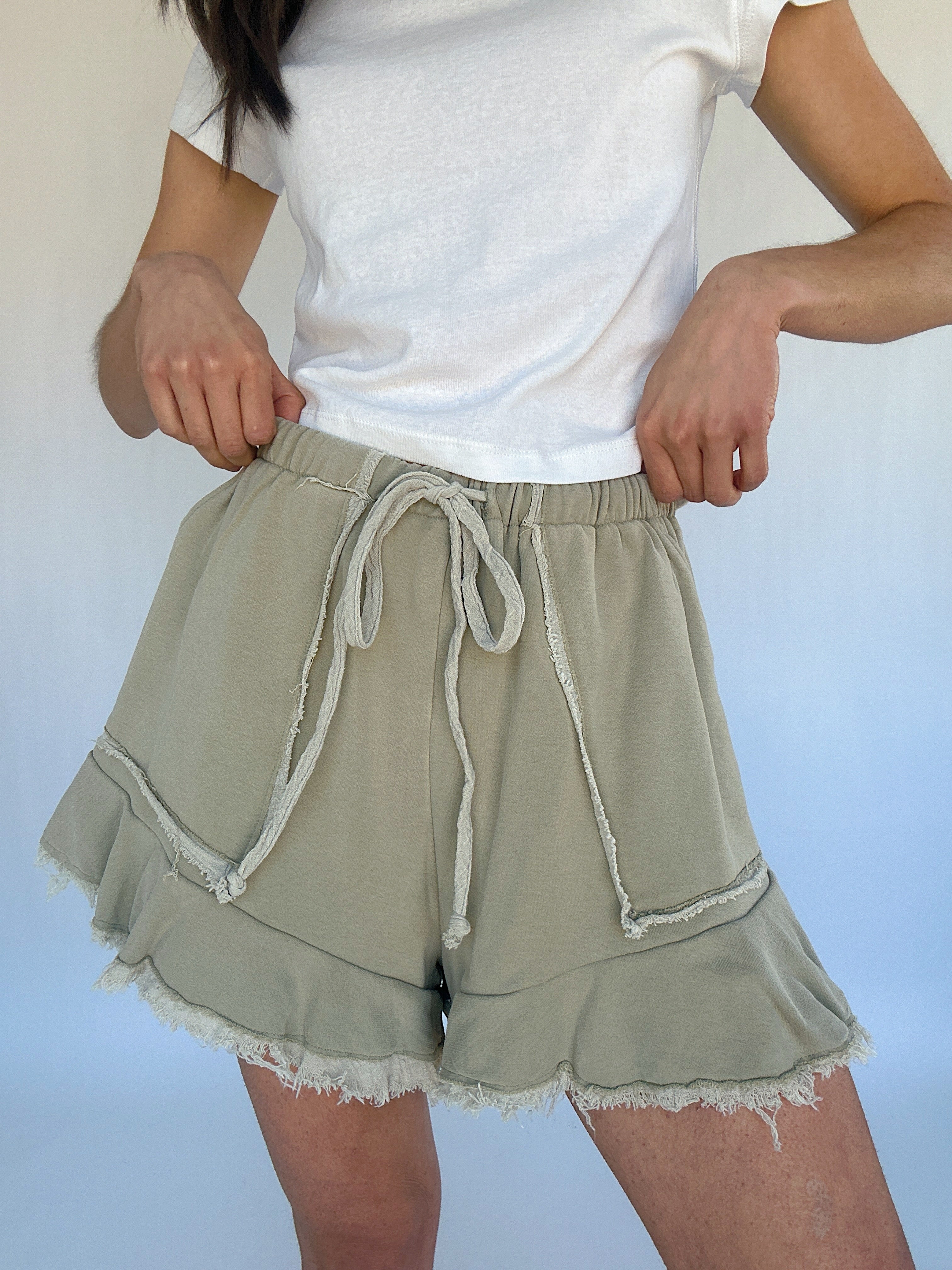 Person wearing a white t-shirt and light green shorts with ruffled hem on a plain background